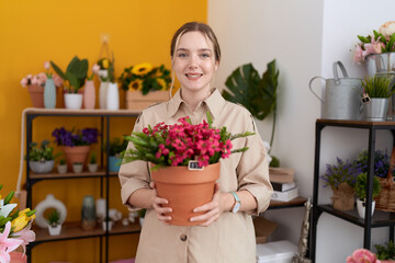 Young caucasian woman working at florist shop holding plant pot smiling with a happy and cool smile on face. showing teeth.