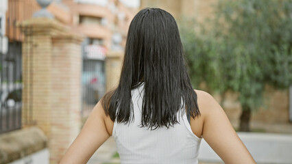A young, beautiful hispanic woman caught in a casual, outdoor portrait, standing backward in a...