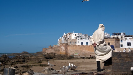 Man in a bernous outside the walls of the medina, seen from the harbor in Essaouira, Morocco