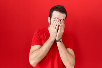 Young hispanic man wearing casual red t shirt rubbing eyes for fatigue and headache, sleepy and...