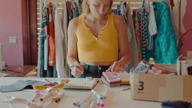 Woman work on slow fashion sustainable clothing brand, small handmade production, design models in small paper notebook in bright and colorful studio