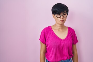 Fototapeta premium Young asian woman with short hair standing over pink background making fish face with lips, crazy and comical gesture. funny expression.