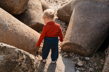 Cute little girl kid toddler between big boulders of rocks by the sea
