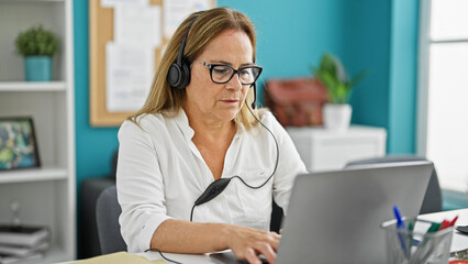 Middle age hispanic woman business worker opening laptop wearing headphones working at the office