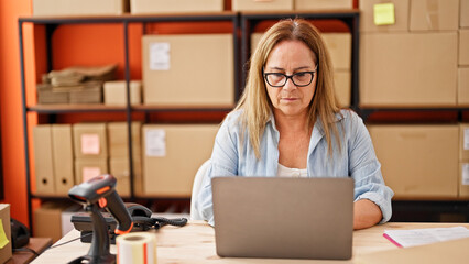 Middle age hispanic woman ecommerce business worker using laptop at office - obrazy, fototapety, plakaty