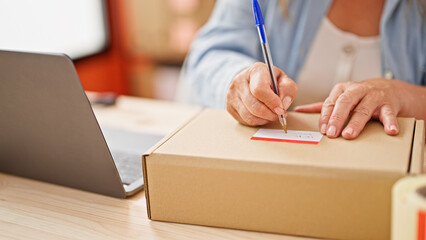 Middle age hispanic woman ecommerce business worker writing on package at office