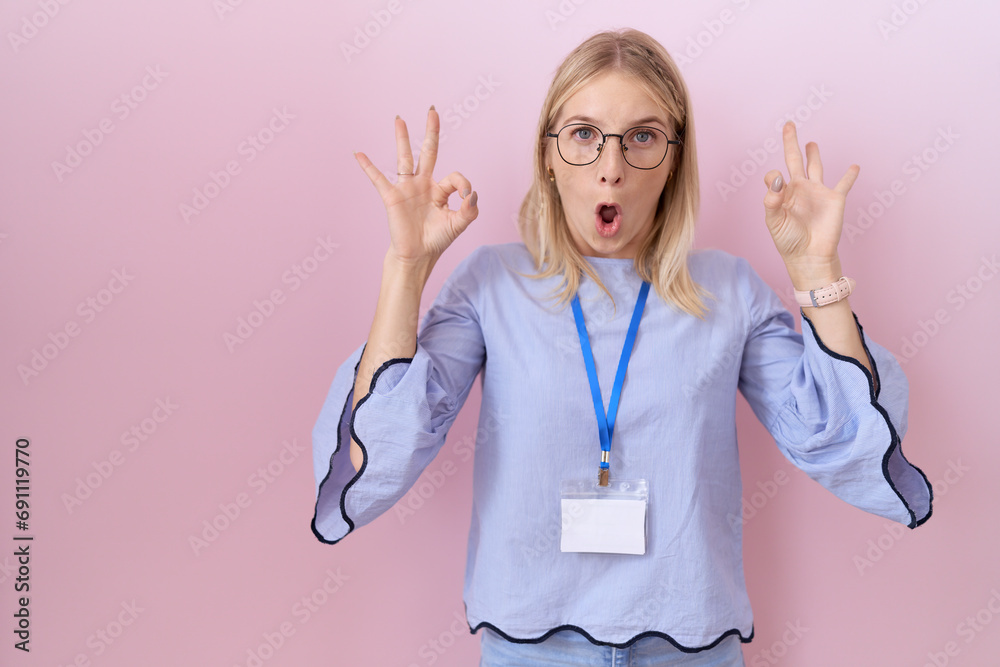 Canvas Prints Young caucasian business woman wearing id card looking surprised and shocked doing ok approval symbol with fingers. crazy expression