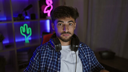 Focused in-game, young arab man, a serious-faced streamer, wearing headphones in a dim gaming room, engrossed in a futuristic virtual gaming world