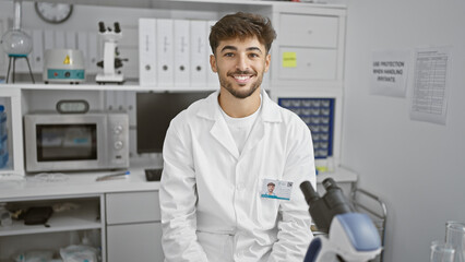 Confident young arab man, a smiling scientist, dives into research in his lab, perfecting his craft with a microscope and immense passion for science