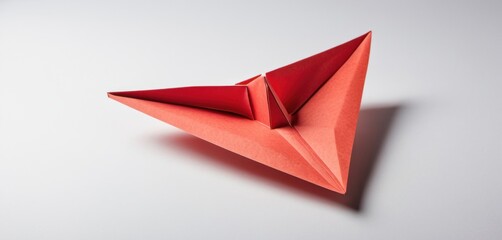  a red origami bird sitting on top of a white table next to a piece of paper that looks like an origami bird.