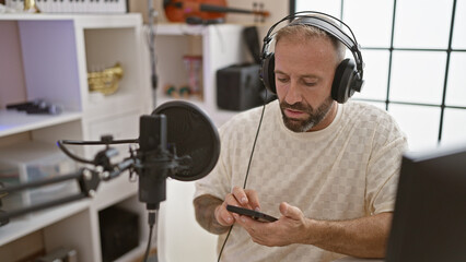 Handsome young man reporter, smiling, presenting live radio show in studio; reading news from smartphone screen, broadcasting information with enthusiasm