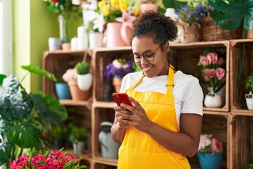 African american woman florist smiling confident using smartphone at flower shop - obrazy, fototapety, plakaty
