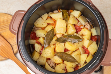 Modern, bright light multi cooker with just cooked stewed potatoes with meat on the kitchen table. Top view of multi cooker with just cooked dish.