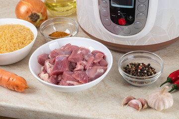 Prepared ingredients for cooking pilaf in modern multi cooker in kitchen on a table. Cooking pilau with meat in multicooker.
