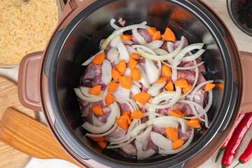 Fries meat with onions and carrots in a multicooker pan. Modern, bright multi cooker with products. Cooking pilaf with meat in multicooker. Top view of multi cooker with vegetables and meat.