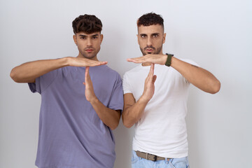Homosexual gay couple standing over white background doing time out gesture with hands, frustrated...