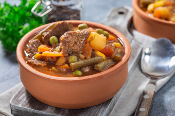 Hearty beef stew with potato, green beans, carrot, peas and corn, in ceramic bowl, horizontal