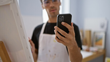 Passionate young hispanic man, an artist, engrossed drawing intricate art on smartphone inside buzzing studio