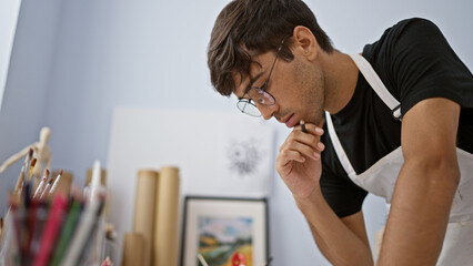 Young hispanice man, an engrossed artist, intensely thinking while drawing at the art studio, doubt...