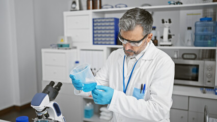 Concentrated young hispanic man, grey-haired and handsome, meticulously measuring liquid for a...