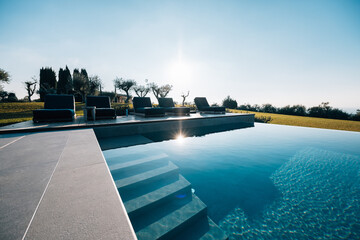 Modern pool with blue water at a luxurious house with deck chairs, trees, and grass in the...