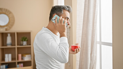 Young, handsome hispanic man with grey hair enjoys morning espresso in his casual home setting,...