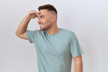 Fototapeta premium Hispanic man with beard standing over white background very happy and smiling looking far away with hand over head. searching concept.