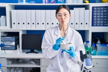 Chinese young woman working at scientist laboratory mixing making fish face with mouth and...