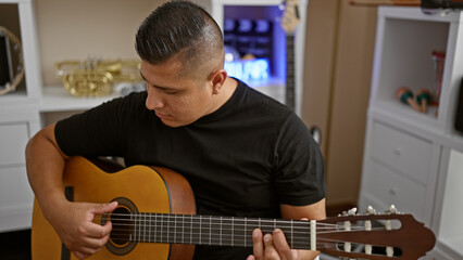 Obraz premium Handsome young latin man immerses soul into playing classical guitar, creating melody magic within club's intimate music studio ambiance