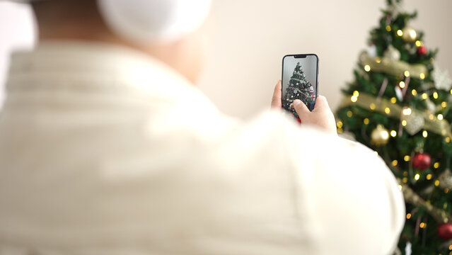Young hispanic man make photo by smartphone to christmas tree at home