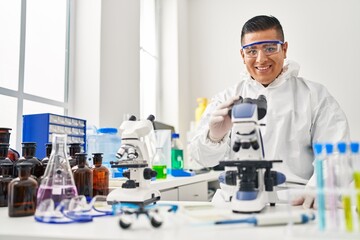 Young latin man scientist wearing covid protection uniform using microscope at laboratory
