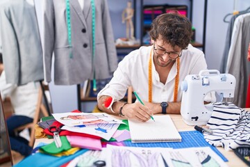 Young hispanic man tailor smiling confident drawing on notebook at clothing factory