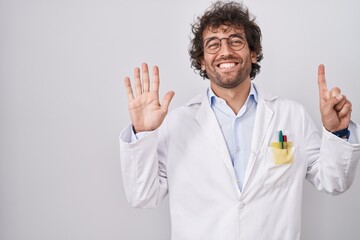 Hispanic young man wearing doctor uniform showing and pointing up with fingers number six while smiling confident and happy.