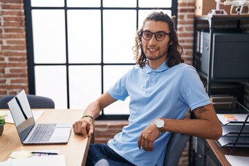Young hispanic man business worker smiling confident sitting on table at office - obrazy, fototapety, plakaty