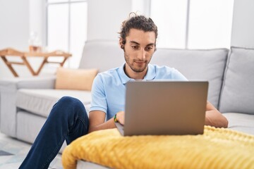 Young hispanic man using laptop sitting on floor at home