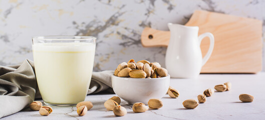 Lactose-free pistachio milk in a glass and nuts on the table web banner