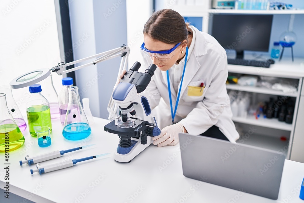 Poster young caucasian woman scientist using microscope at laboratory