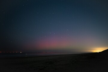 Purple coloured northern lights or aurora borealis under a starry sky on the North Sea beach