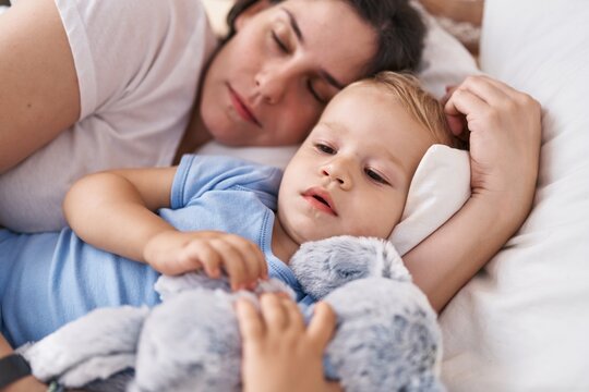 Mother and son sleeping on bed hugging doll at bedroom