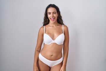 Fototapeta premium Young hispanic woman wearing white lingerie winking looking at the camera with sexy expression, cheerful and happy face.