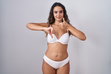 Young hispanic woman wearing white lingerie doing thumbs up and down, disagreement and agreement expression. crazy conflict