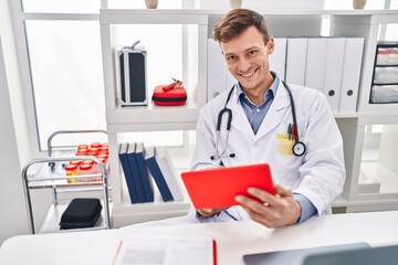 Young man doctor using touchpad sitting on table at clinic