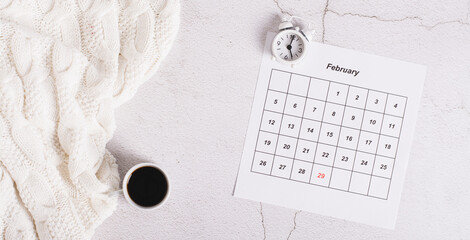 Leap year concept, calendar, alarm clock and coffee on light top view web banner