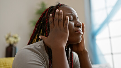 Depressed african american woman with braids sitting alone on sofa at home, unhappy expression...