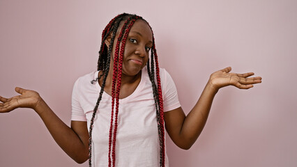 Clueless african american woman with braids, standing unsure over a pink isolated background,...