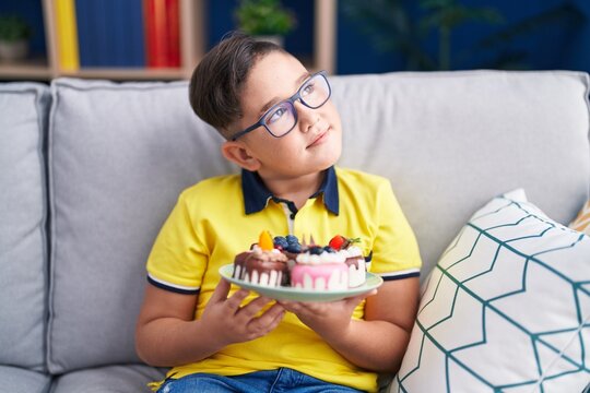 Young Hispanic Kid Holding Cake Sweets Smiling Looking To The Side And Staring Away Thinking.