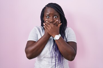 Young african woman standing over pink background shocked covering mouth with hands for mistake....