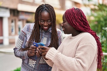 African american women friends using smartphone and credit card at street