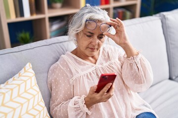 Middle age grey-haired woman looking screen smartphone with vision problem at home