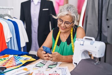 Middle age grey-haired woman tailor smiling confident using smartphone at tailor shop